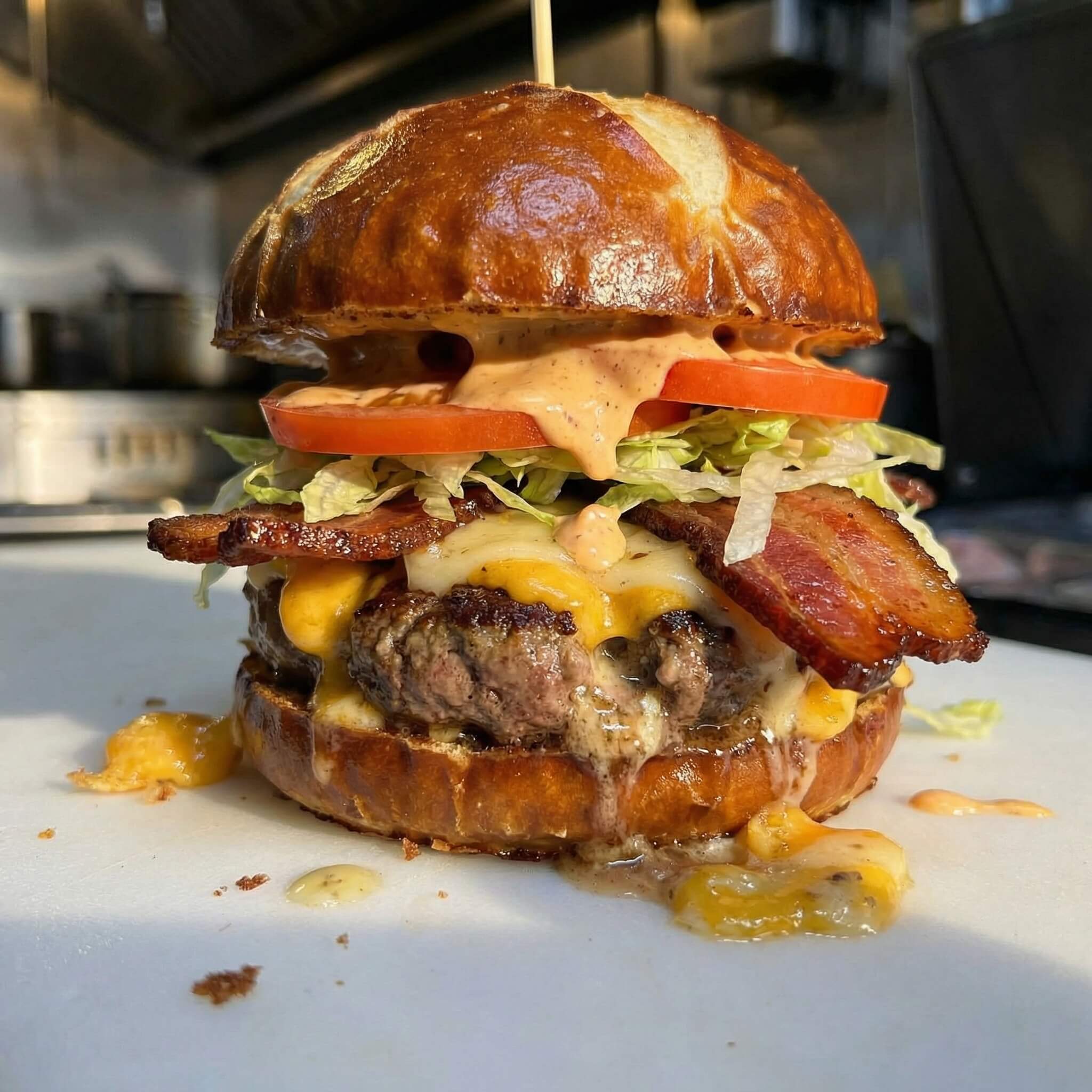 Burger stuffed with garlic. On the burger is cheddar cheese curds, pepperjack, bacon, lettuce, tomato, chipotle mayo, on a pretzel bun.