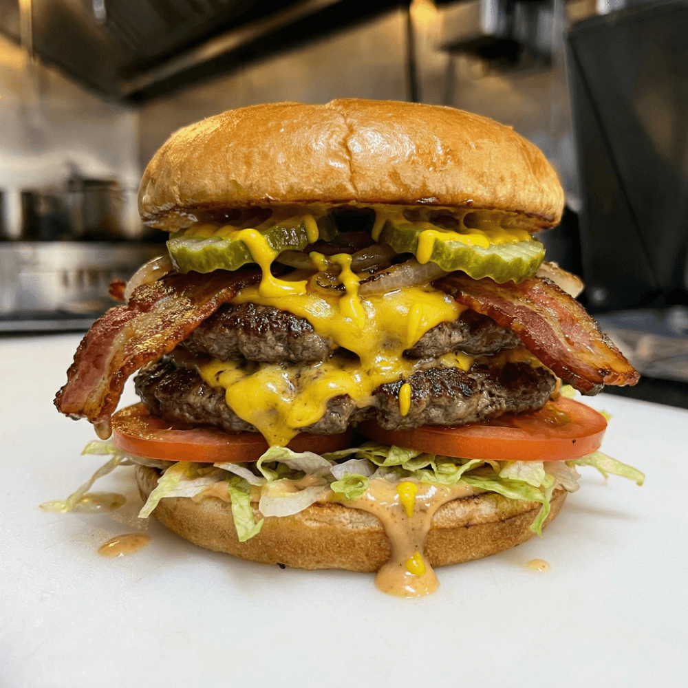Double patty, double cheddar cheese, double bacon, lettuce, tomato, onions pickles and mustard on a house bun